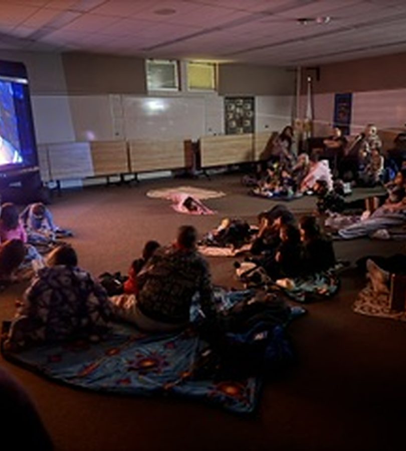 Children and families seated on blankets in a darkened room watching an animated film on a big screen.