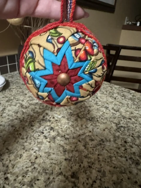 A red and blue star ornament held in a hand, photographed from above against a patterned floor.