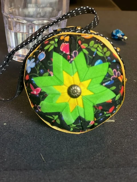 A bright green and yellow star ornament with a beaded black hanger coiled beside it.