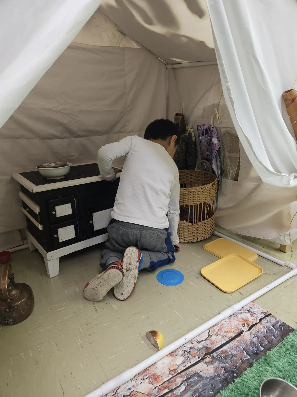 A child crouched inside a canvas tipi set up in the classroom, sorting things on the floor.