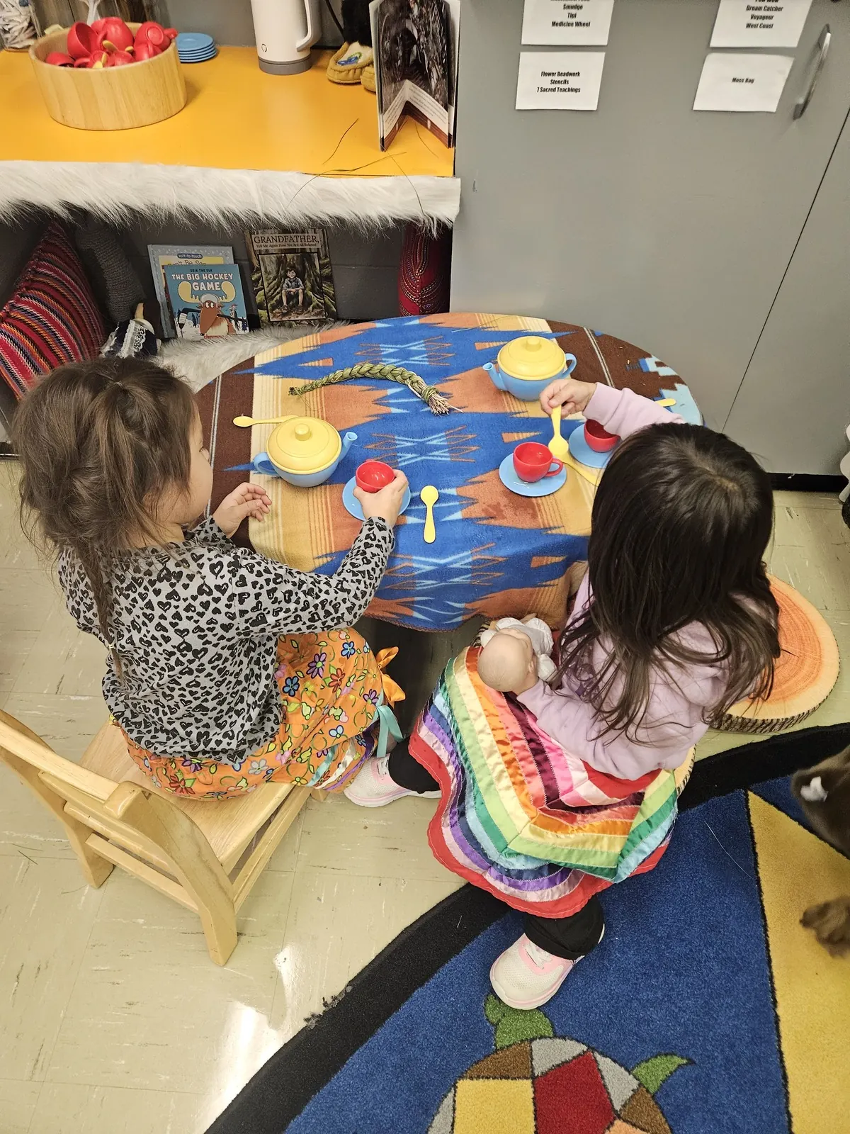 Two children at a painted round table, a hand drum resting on it between them.