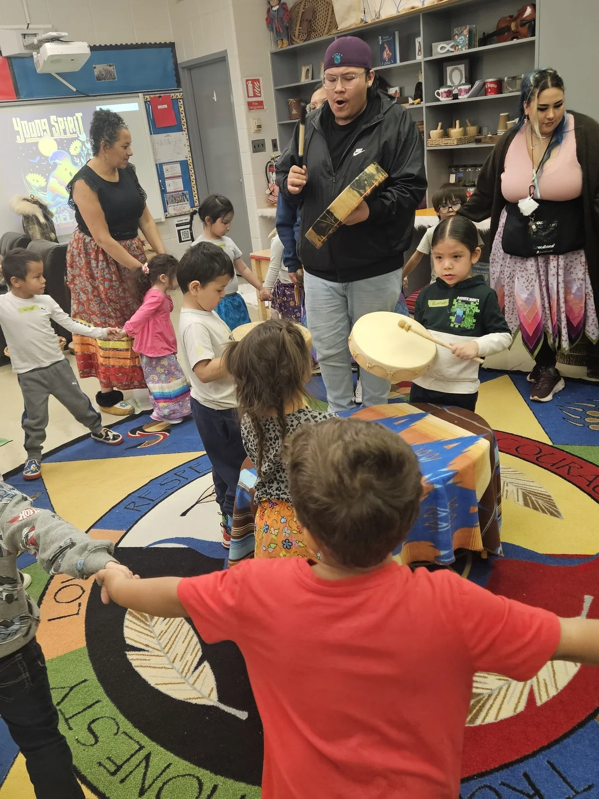 A child in a red shirt drumming at the front of the group.
