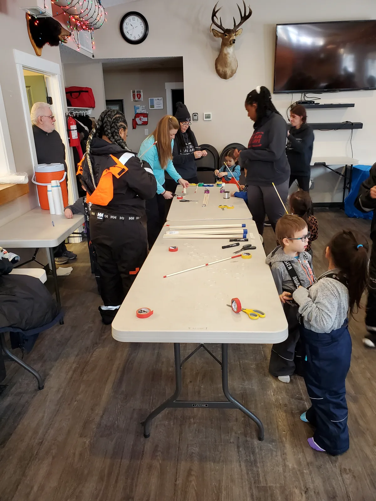 Wooden fishing rods laid out along a table while children and adults get them ready.
